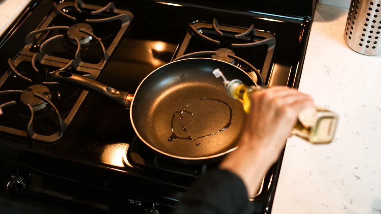 Olive oil being poured into a non-stick pan over gas stove