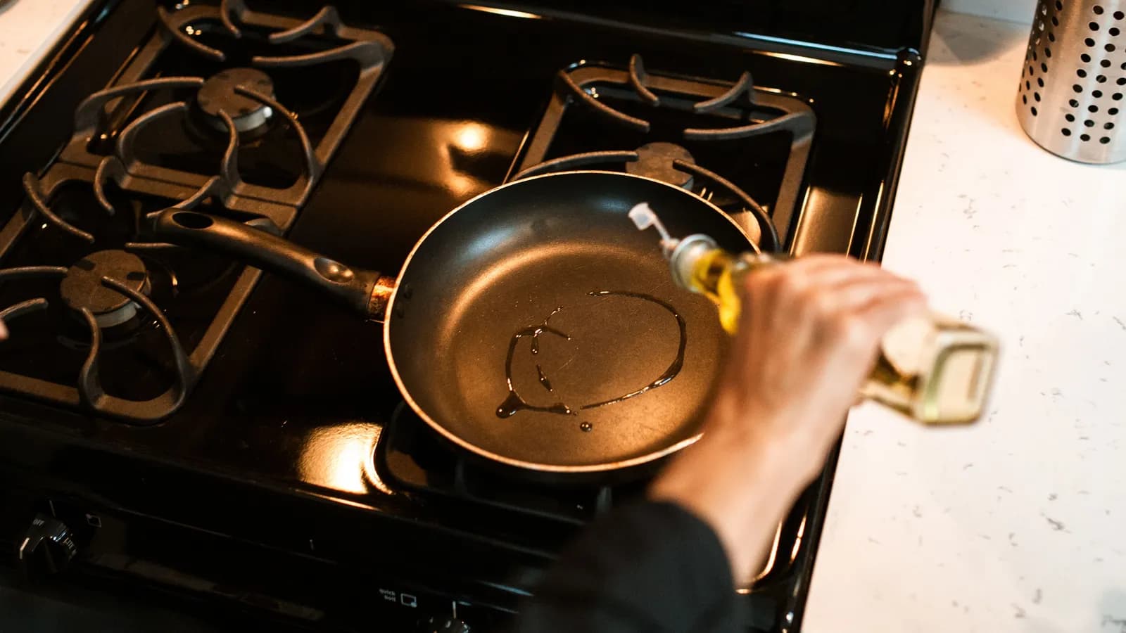 Olive oil being poured into a non-stick pan over gas stove