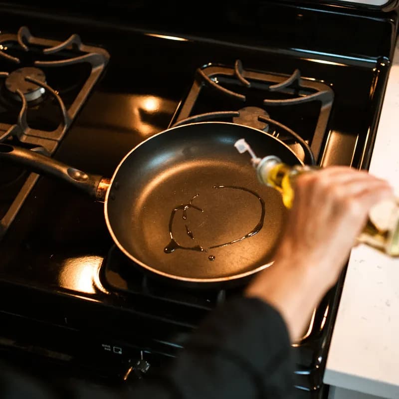 Olive oil being poured into a non-stick pan over gas stove