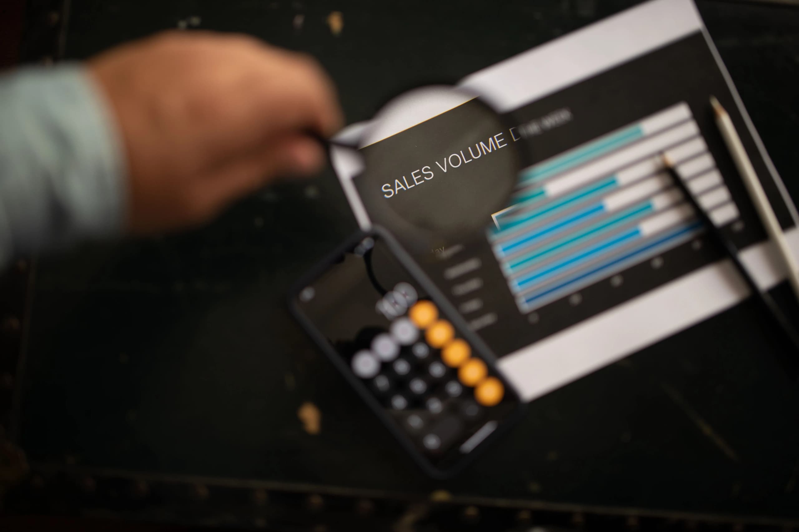 Person reviewing sales volume charts and financial data with a calculator on a desk.