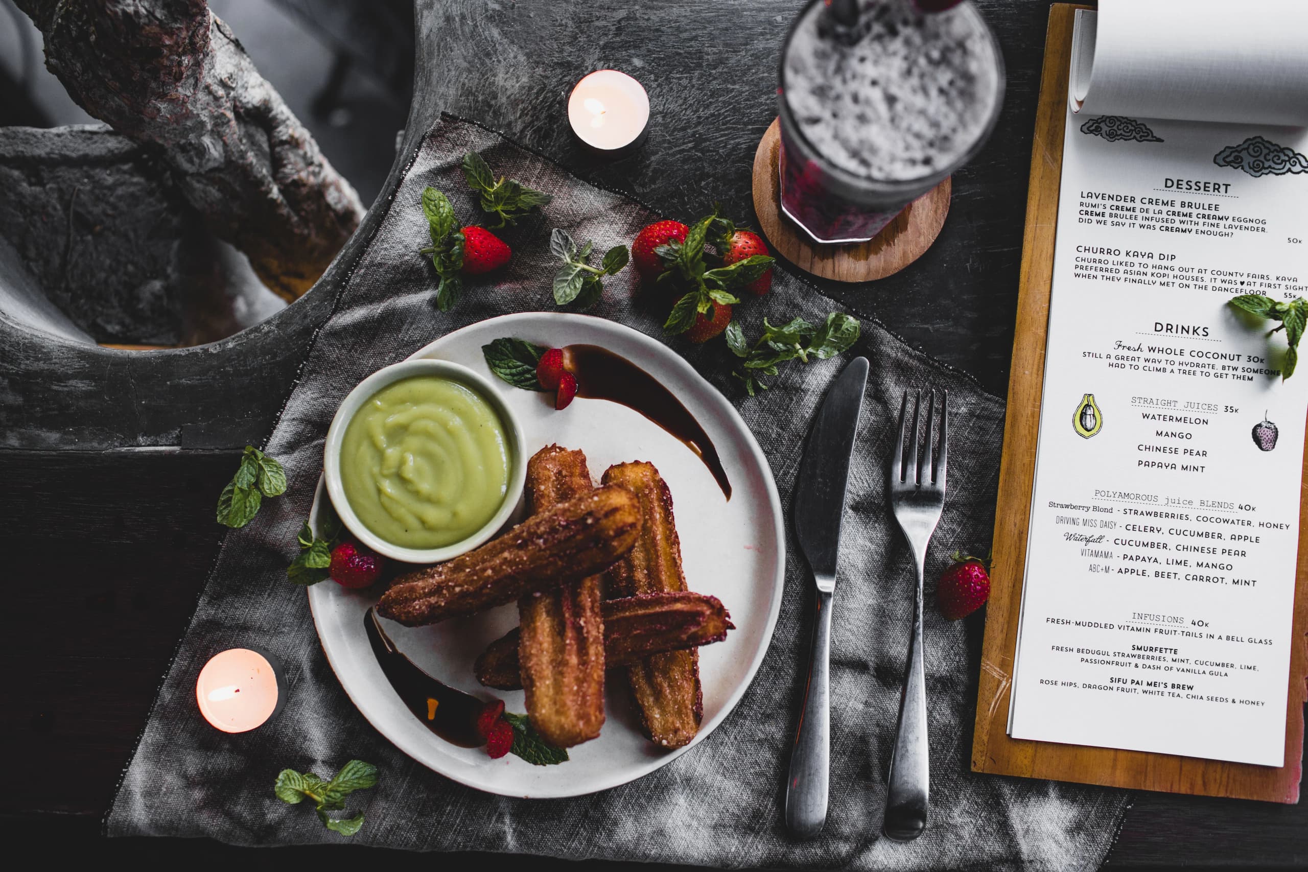 Plate of churros with avocado dip, surrounded by strawberries and candles, perfect for a cozy dining setting.