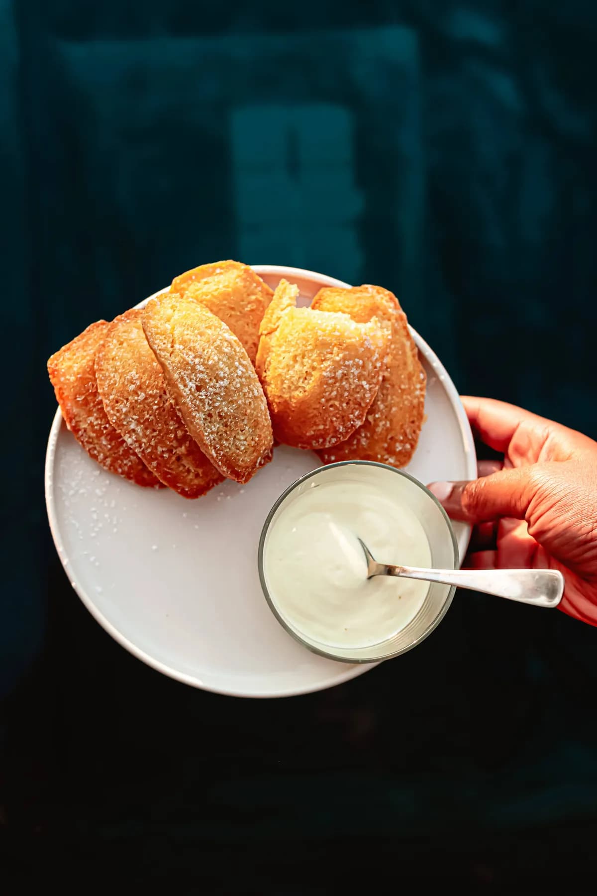 Madeleines pictured by the water with a hand holding whipped cream.