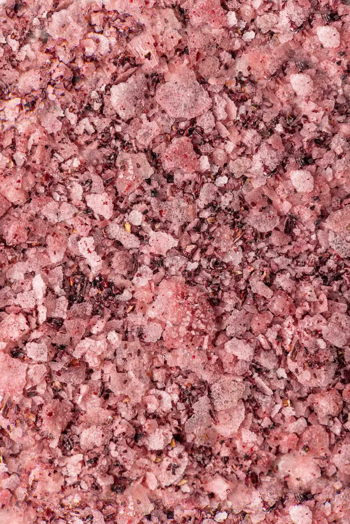 Close-up of pink Shiraz and hibiscus salt crystals with visible hibiscus pieces.