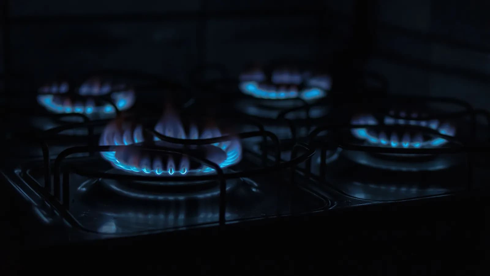 Four pans cooking different foods over gas burners at different heat levels