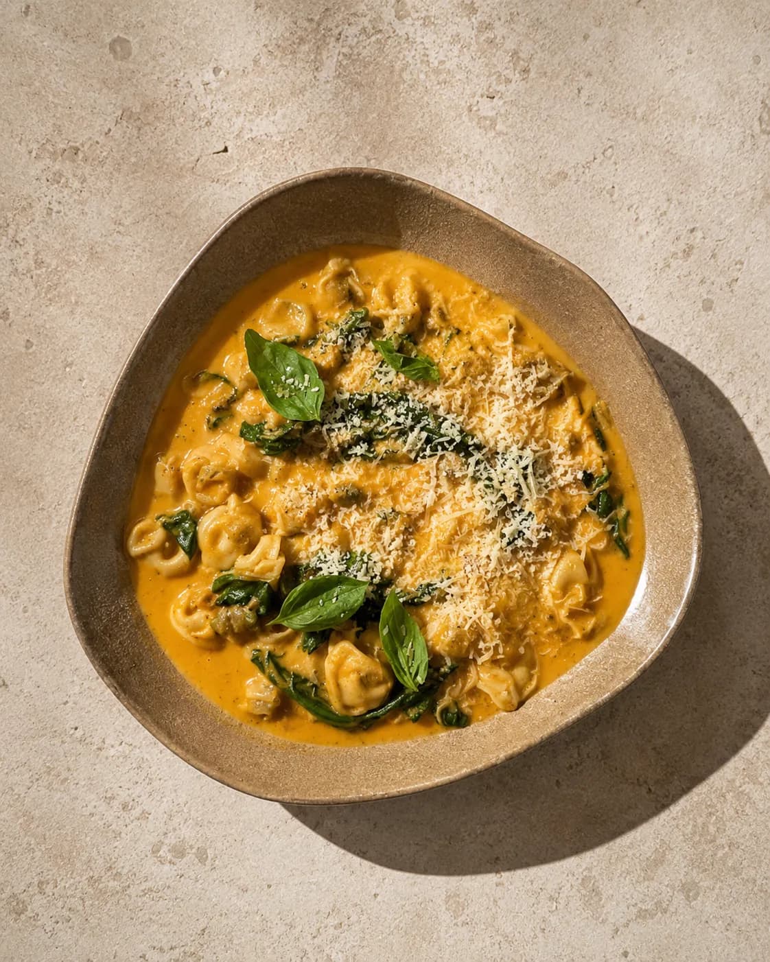 Creamy tortellini with spinach in a tomato cream sauce, topped with grated Parmesan and fresh basil.