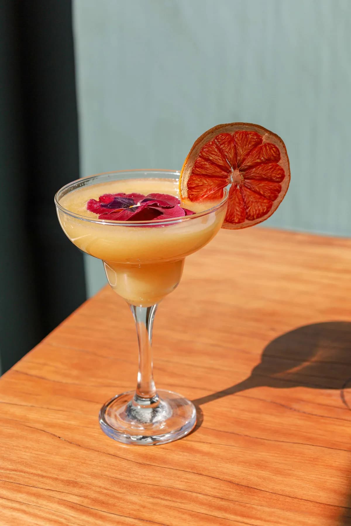 Cocktail garnished with dried citrus and edible flowers on a wooden table.