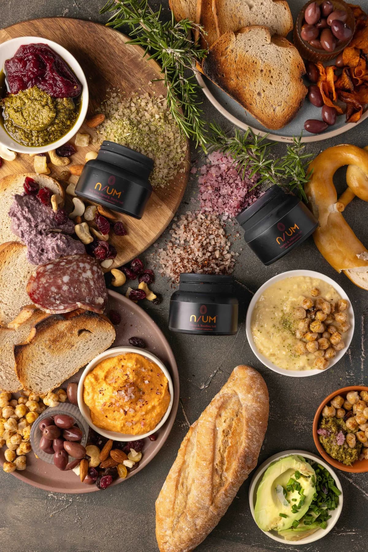 Canapé board with breads, salami, hummus and accompaniments styled with a selection of artisanal salts.
